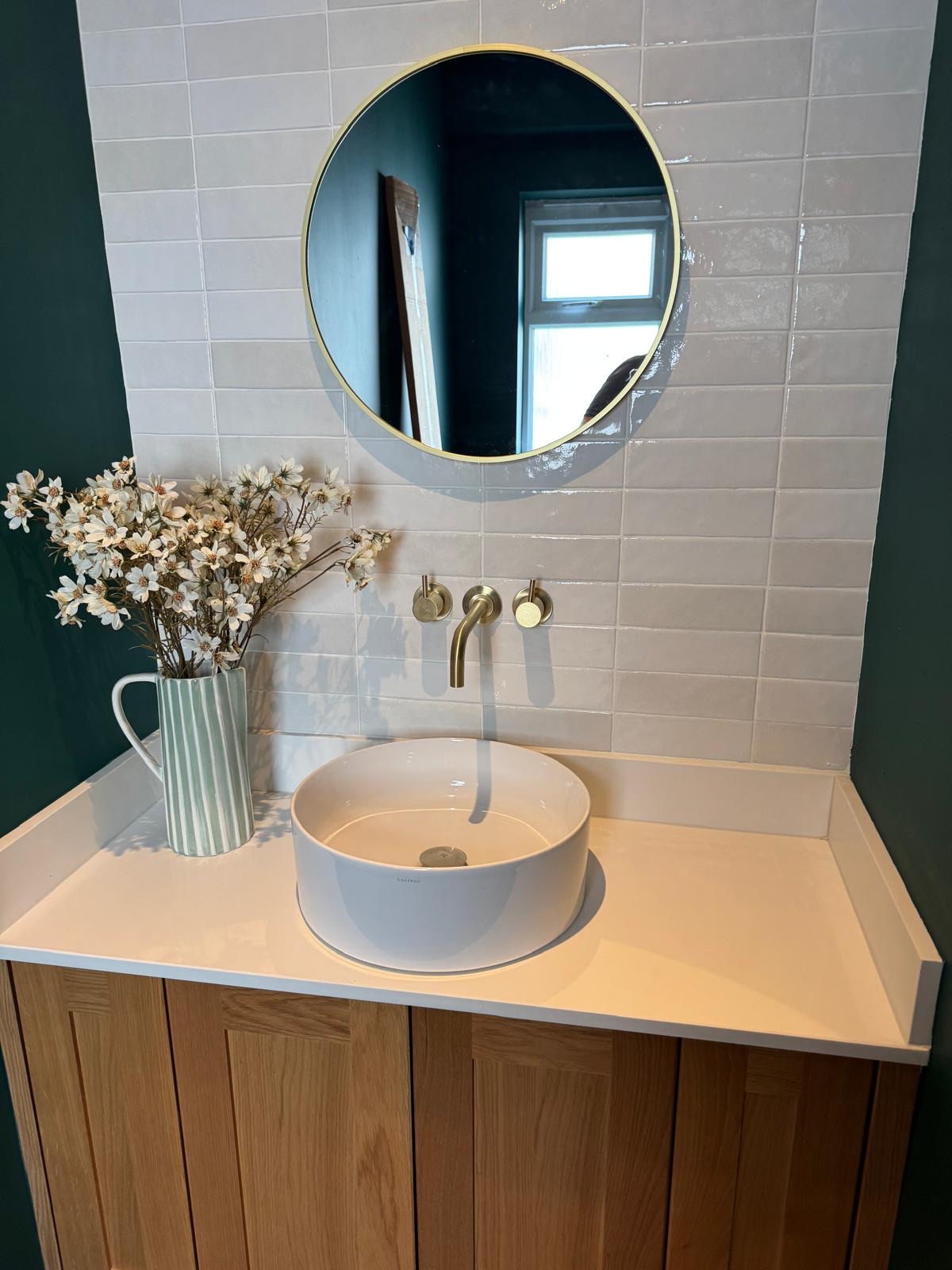 Oak vanity with white worktop, vessel basin, brushed brass tap and round mirror